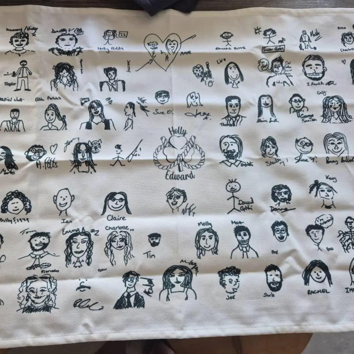 Cream tea towel printed with black ink guest self-portraits and a heart motif